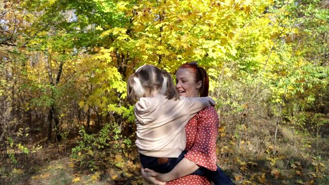 a red-haired happy woman with a little daughter in her arms in an autumn sunny park