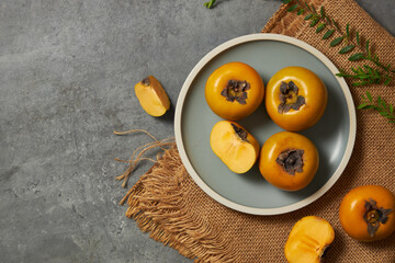 Top view of persimmon in grey plate , flower , green leaf , brown shawl with grey background and blank space for advertising 