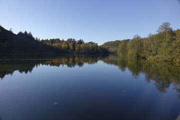 Autumn trees with colourful foliage reflecting in the water under a blue sunny sky, Schöntalweiher, Ludwigswinkel, Fischbach, Rhineland Palatinate, Germany
