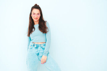 Obraz premium Young beautiful smiling female in trendy summer hipster clothes. Sexy carefree woman posing near light blue wall in studio. Positive model having fun indoors. Cheerful and happy