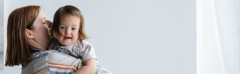 Woman holding toddler daughter with down syndrome at home, banner.