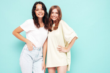 Two young beautiful smiling brunette hipster female in trendy summer clothes. Sexy carefree women posing near blue wall. Positive models having fun. Cheerful and happy