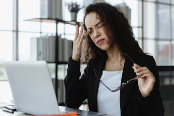 young woman feels eye strain and fatigue holding glasses, rubbing her eyes, irritated after working at a computer for a long time.
