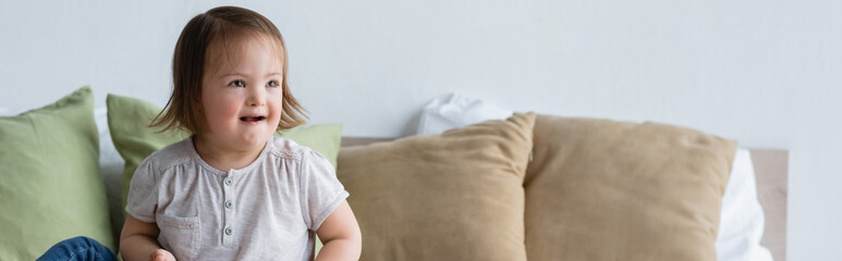 Fototapeta premium Smiling toddler girl with down syndrome looking away on bed, banner.