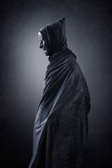 Fototapeta na wymiar Spooky figure with hooded cape over dark misty background