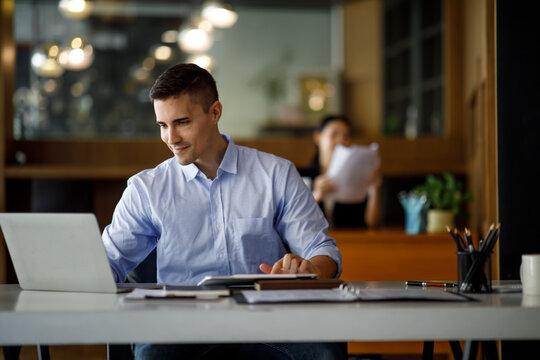 Smiling businessman working on a laptop computer in a modern office,doing finances, accounting analysis, report data pointing graph Freelance education and technology concept.