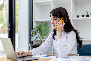 Obraz premium Beautiful Asian businesswoman talking on mobile phone and using laptop, concept image of Asian business woman working smart, modern female executive, startup business woman, business leader woman.