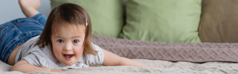 Toddler kid with down syndrome looking at camera on bed, banner.