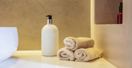 Fototapeta na wymiar Bathroom interior detail. Clean hand towels roll ups, soap dispenser and sink basin on a table