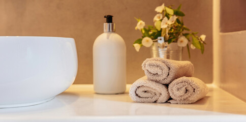 Bathroom interior detail. Clean hand towels roll ups, soap dispenser and sink basin on a table