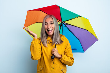 middle age gray hair woman feeling happy and astonished at something unbelievable. umbrella and...