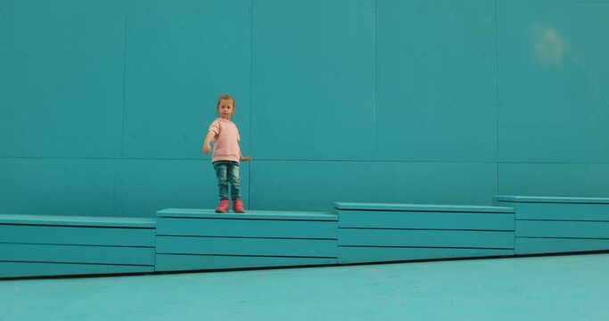 Cute shy little girl kid dancing outside on blue background. Funny preschooler child showing danceon street stage