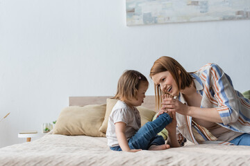 Woman holding feet of daughter with down syndrome on bed.