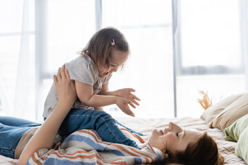 Mother playing with cheerful baby daughter with down syndrome on bed.