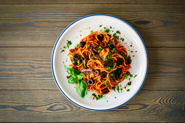 Pasta puttanesca with tomato sauce, anchovies, chili, capers and olives on wooden table
