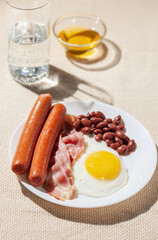 Eggs with bacon, sausages and beans in a plate on the table. Hard sunlight
