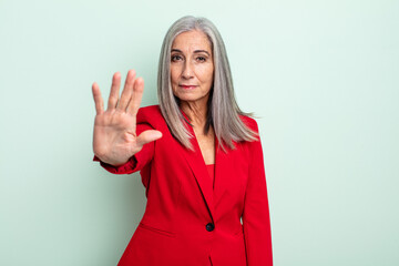 middle age gray hair woman looking serious showing open palm making stop gesture. senior...