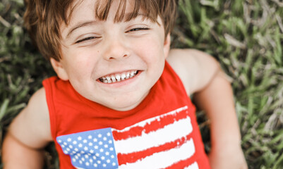 little boy playing on the backyard on a little slide with an American shirt 4th of july 