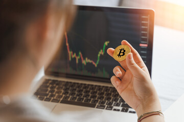 Businesswoman, investor, trader hold Bitcoin Cryptocurrency, using computer laptop with graph chart, trading stock market, investing Bitcoin cryptocurrency at home. Investment and technology concept.