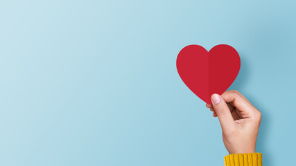 Woman hand holding red paper heart on blue background. Concept of valentines day, love, and donate