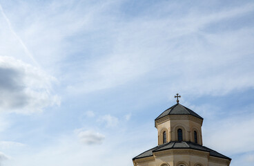 Dome of a Georgian Orthodox cathedral with a cross against a blue sky with clouds.