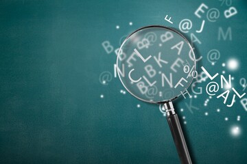 A magnifying glass with part of scattered English alphabet letters on the desk background - obrazy, fototapety, plakaty
