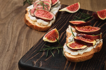 Toast with figs and cream cheese on a wooden board for serving, closeup view, selective focus. Snack idea, before dinner. Close-up on healthy food