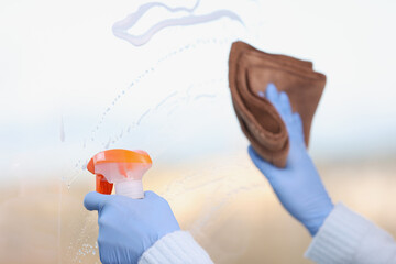 Cleaner washing window with microfiber cloth and spray with detergent closeup