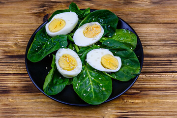 Spinach leaves and halved boiled eggs on a black plate