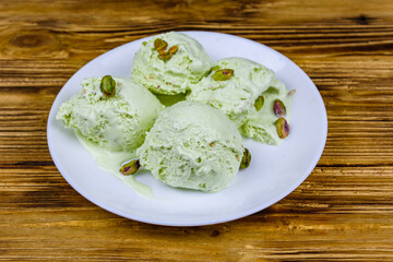 Glass bowl with pistachio ice cream balls and nuts on a wooden table
