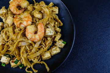 Black plate with pad thai on a slate board. Top view