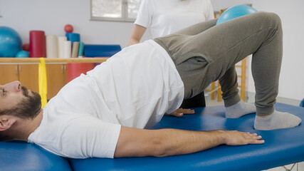 Man doing bridge and squeeze exercise, using ball. Physiotherapy exercise with the ball between the knees for the inner thighs and good leg alignment.