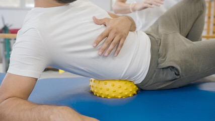 Man using a spiky massage ball to release tight hips. Laying on the ball under the right hip, and rolling over it in a waist and low back.