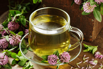 Red clover tea in glass cup on wood on rustic background, herbal drink is good for menopause, bone, heart health and for skin and hair care, closeup, naturopathy and natural medicine concept