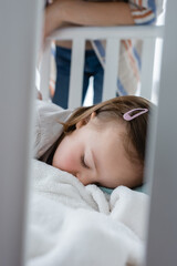 Child with down syndrome sleeping in baby crib near mother.