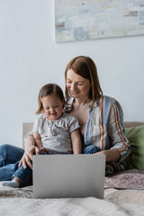 Mother hugging daughter with down syndrome near laptop on bed.