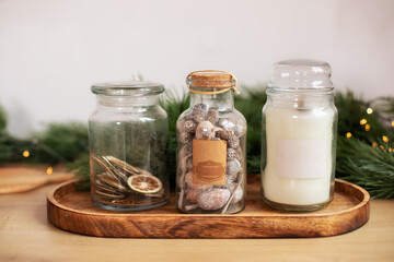 Glass jars with some aromatic spices and candle on an old wooden stand. Jar of dried sliced citrus fruits, Fir branch, Christmas spices and decor. Winter holidays, New Year or Christmas concept. 