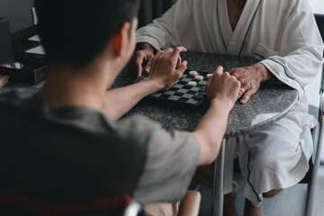 Hands of young man with disability smiling face looking and playing a checkers on a table with father in bedroom at the home.
