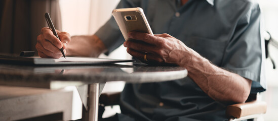 Hands of senior man with disability holding a pen to writing something with business working or sign name on important document by himself on desk in home office, People work and using phone concept.