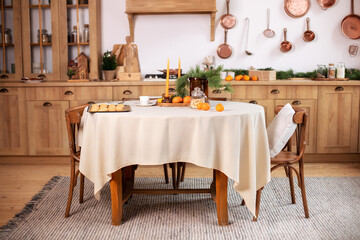 Interior design scandinavian kitchen with round table and chairs. Stylish dining room in rustic style. Cozy Wooden kitchen decorated Christmas or new year. On table fir branche in vase, Xmas cookies	