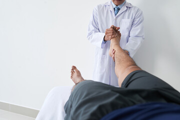 Horizontal shot of unrecognizable osteopathic physician working with male patient holding his leg doing foot joint manipulation