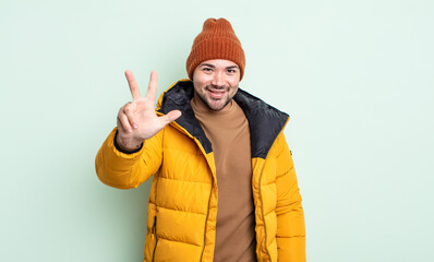 young handsome man smiling and looking friendly, showing number three. cold weather concept
