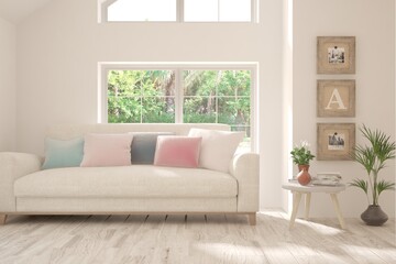 Fototapeta premium White living room with sofa and summer landscape in window. Scandinavian interior design. 3D illustration