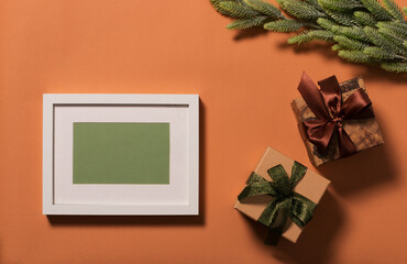 White frame with green background for the inscription. Branches with green needles are decorated with a red star. Two gift boxes are decorated with bows. Christmas background. View from above.