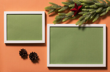Two white frames with a green background for the inscription on the red surface. Spruce branches are decorated with a red star. Christmas background. View from above.