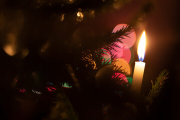 A lit white candle in a Christmas tree with colorful large bokeh circles in the background