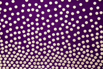 Golden dots on a dark background. Purple background with polka dots, fabric texture with a pattern.