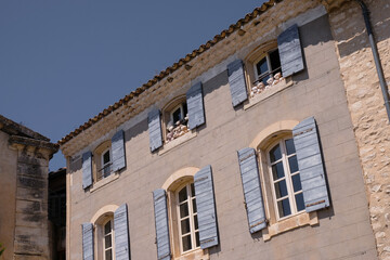 Fototapeta na wymiar Beige facade of an old house with pale cornflower blue color shutters decorated with bears in the windows. Wooden shutters and sky of the same color. Travel and tourism concept.