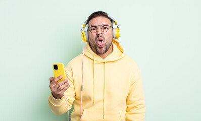young handsome man feeling disgusted and irritated and tongue out. headphones and smartphone concept