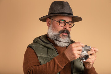 bearded photographer with glasses looking at vintage camera on light brown background